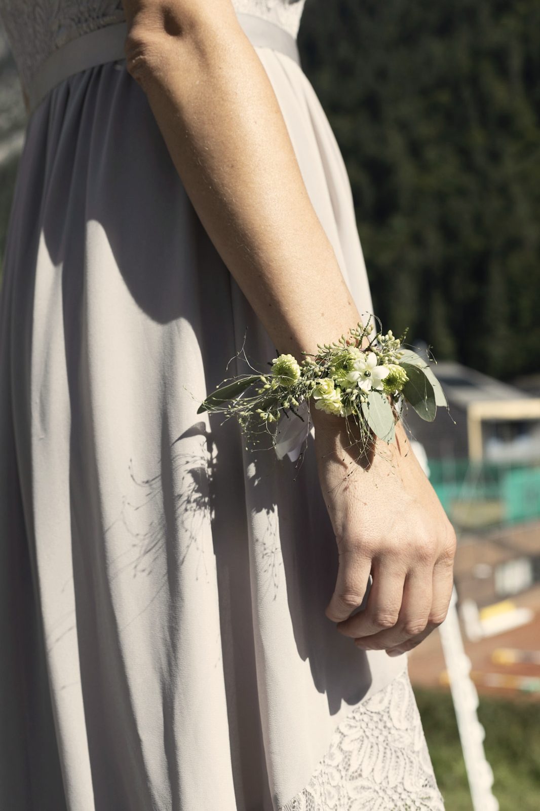 Ein Blumenarmband am Handgelenk, der Hang dahinter.