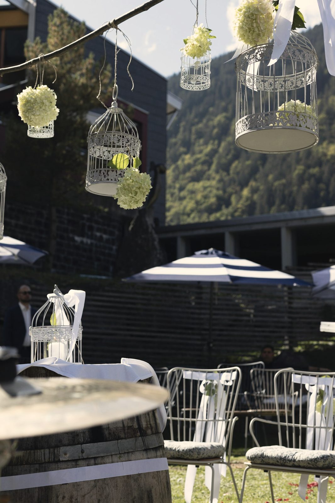 Vogelkäfige mit Blumen über der Terrasse des Walliserhofs, dahinter der Hang